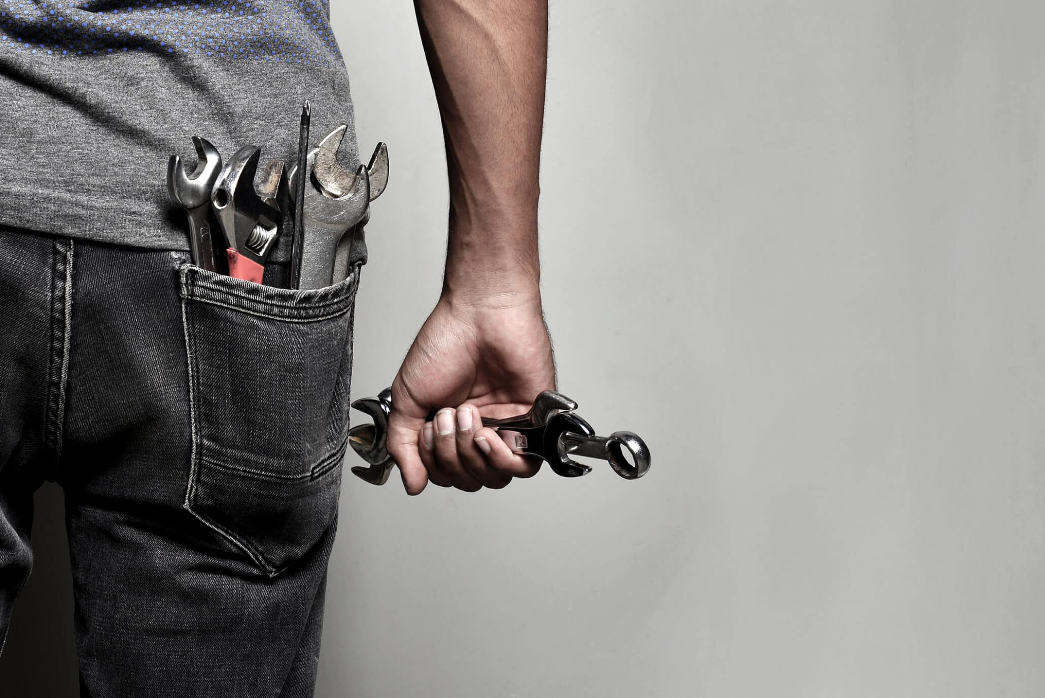 Detail von einer Hosentasche und Hand mit Schraubenschlüsseln