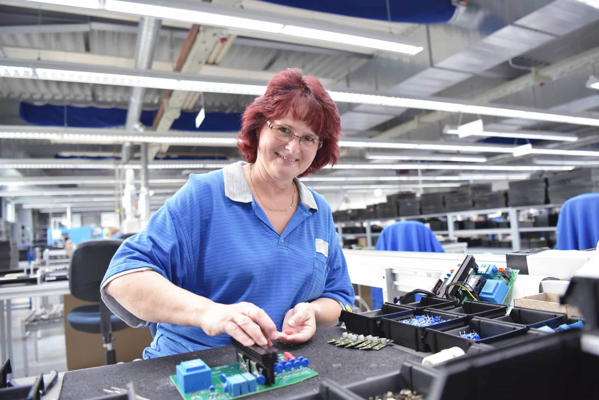 Lächelnde Frau bei ihrem Zeitarbeitseinsatz in einer Fertigungsfabrik beim Prüfen von Mikro-Elektronik