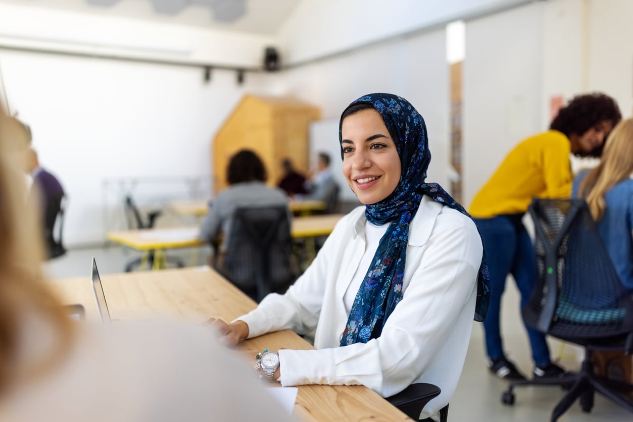 Portrait einer jungen Frau an ihrem Arbeitsplatz in einem Großraumbüro