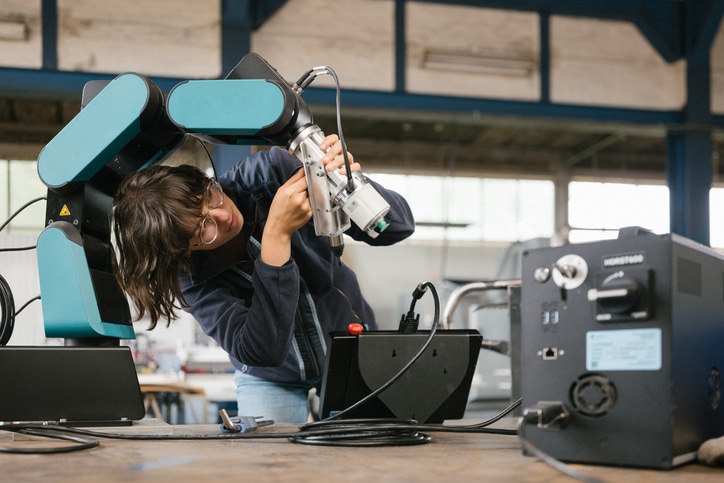 Junge Frau schraubt als Elektrikerin an einer Maschine während ihres Zeitarbeiteinsatzes