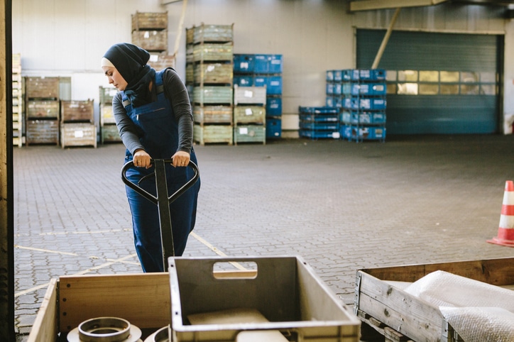 Junge Frau bewegt eine Palette in einem Lager während ihres Zeitarbeitseinsatzes