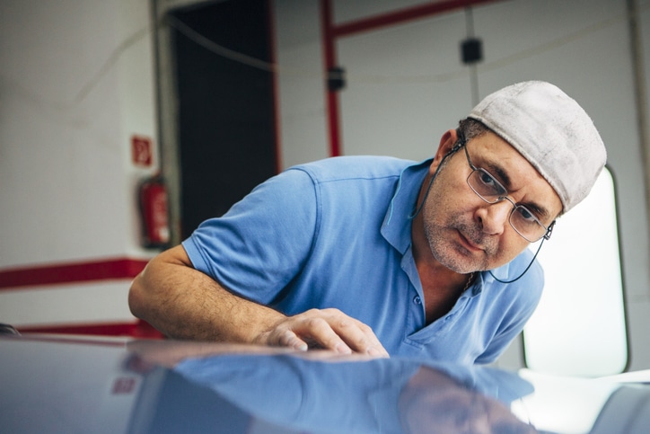 Portrait eines älterern Mannes bei der Inspektion seiner Lackier-Arbeit in einer Industriehalle