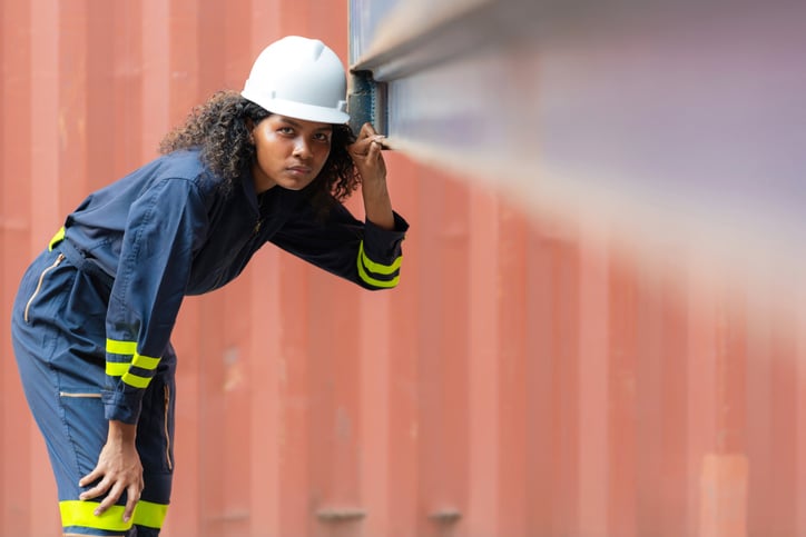 Portrait einer jungen Frau mit Schutzhelm die im Hamburger Hafen einen Container kontrolliert