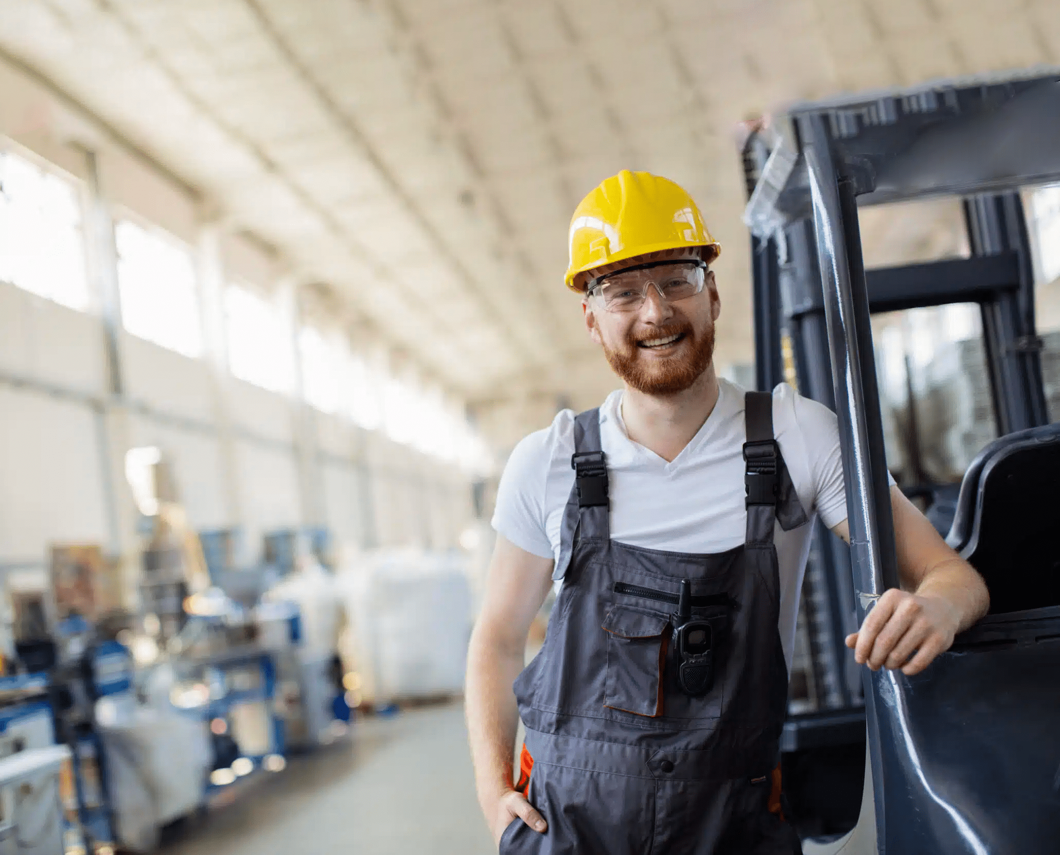 Junger Mann mit gelbem Schutzhelm lehnt an einem Gabelstapler