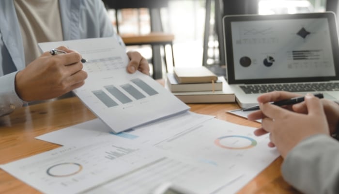 Detail eines Schreibtisches mit Laptop und Analysecharts und dem Anschnitt zweier Personen als Personalverantwortliche bei der Anforderungsanalayse zur Potenzialanalyse